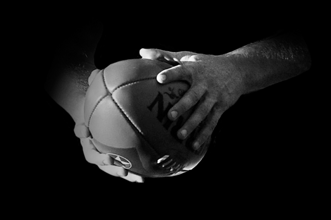 Sherrin AFL ball held in two hands black and white